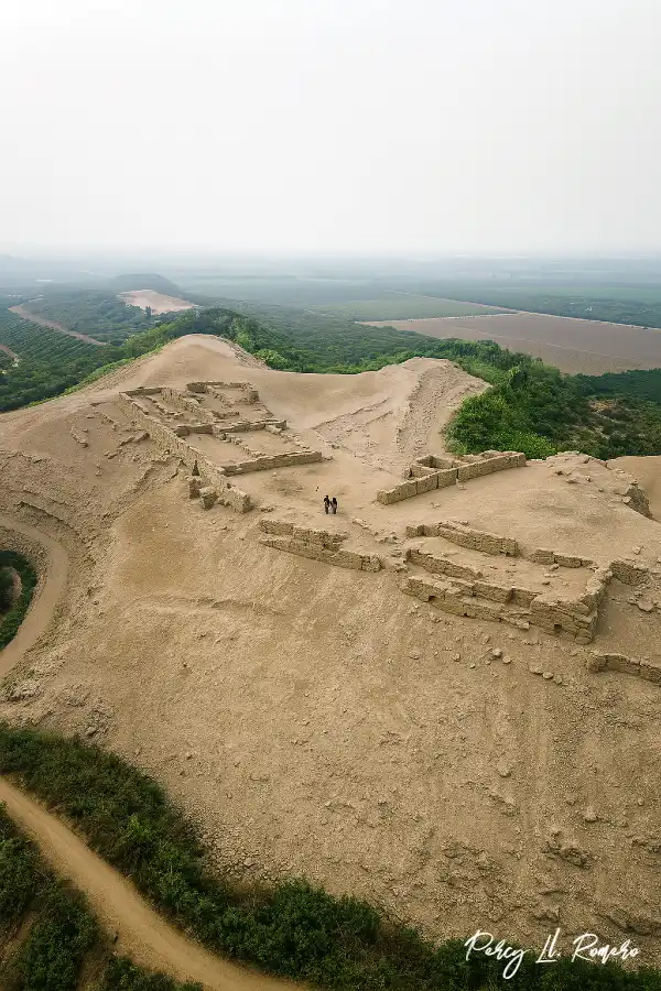 Vista aérea de la Fortaleza de Ungará en Imperial, Cañete, con estructuras prehispánicas de adobe sobre una colina rodeada de campos agrícolas verdes